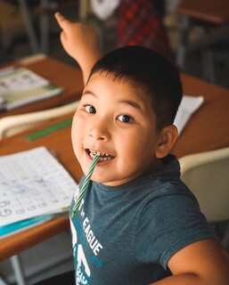 A boy in the primary grades bites a pencil while he works on writing his letters.