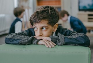 A young boy with a pensive expression leans on the back of a green couch.