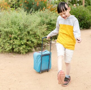 Happy child pulling a blue suitcase in a garden, enjoying a sunny day outdoors.