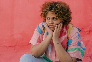 Young woman with curly hair looks thoughtful against a bright pink backdrop